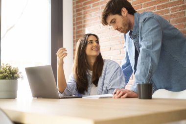 Evde çalışan modern bir çift notlar ve dizüstü bilgisayarla mutlu bir şekilde gülümsüyor. Genç adam ve kadın ofiste bilgisayar ve kablosuz internet bağlantısı kullanarak eğleniyorlar. Küçük işletme konsepti yaşam tarzı