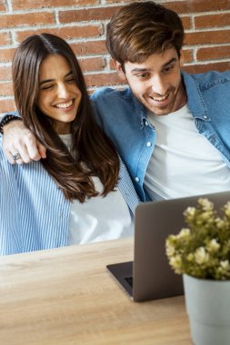  Ev ofisinin masasındaki masada, açık bir bilgisayarın önünde yüzünde heyecan ifadesi olan bir kadın ve erkek. Kazanan başarı duygusunu içeride hisseder.