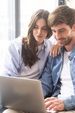 Pazar öğleden sonra evdeki kanepede rahat rahat oturan mavi kot giysili çift dizüstü bilgisayar kullanıyor. Ev içi boş zamanlarında online aktivitelerde çalışan insanlar. Kablosuz