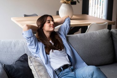 Rahatlamış bir insan evdeki oturma odasında pencereli bir kanepede oturmuş gülümsüyor. 