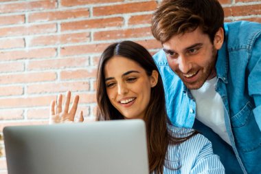 Çift, evdeki masada arkadaşlarıyla görüntülü konuşma yapıyor. Modern insanlar online sohbet konferansında. Küçük bir internet işi. Uzaktan kumandalı ebeveynlere merhaba demek. Kadın ve erkek boş vakitlerinde dizüstü bilgisayar kullanıyor.