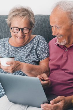 Senior retired happy couple embracing using laptop together, smiling elderly family reading news, shopping online at home, older people and computer or good vision after laser correction concept