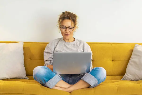 Woman Smiling Using Laptop Computer Home Sitting Comfortably Yellow Sofa – stockfoto