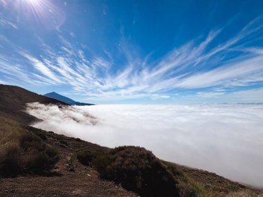 Arka planda dağ manzaralı güzel bir manzara ve öndeki tepede bulutlar. İnanılmaz bir seyahat manzarası var. Mavi gökyüzü ve vahşi doğa