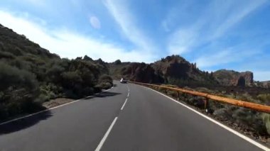 Dağ manzaralı yol boyunca araba sürüyorum. Güzel, boş bir yoldan geçen bir kameranın görüntüsü. Ulaşım ve sürücü bakış açısı kavramı. Dağ yolculuğu. Arka planda mavi gökyüzü