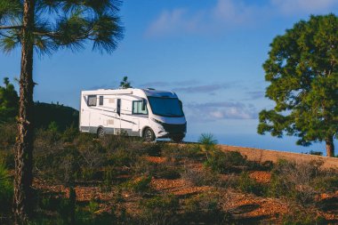 Modern motorhome camper van parking in the nature with trees and mountains around for free park camping alternative garden home and destination for holiday vacation. Living alone off grid traveler clipart