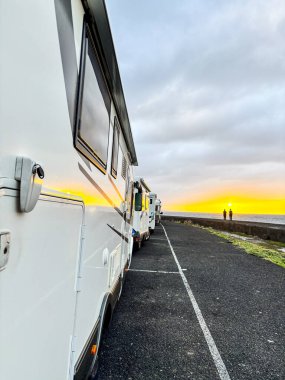 Birçok karavan karavanı gün batımı manzaralı yolda park ediyor. Alternatif seyahat ve tatil konsepti Vanlife yaşam tarzı. Modern eğlence minibüsüyle seyahat