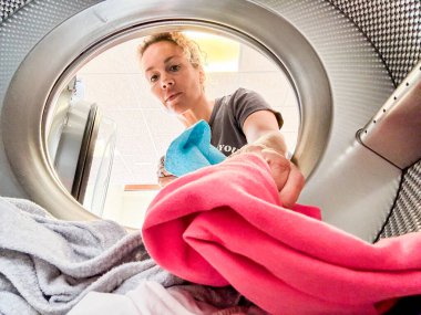 Çamaşır yıkayan kadın çamaşır makinesinin içinde. Yetişkin bir kadın ev ödevinde ya da otomatik çamaşırhanede renkli giysiler yıkıyor. İş yerindekiler