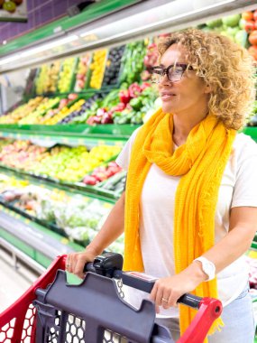 Alışveriş arabalarını iten ve süpermarkette raflardan meyve toplayan güzel bir kadın. Marketten yiyecek almak..