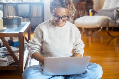  Yetişkin bir kadın dizüstü bilgisayarla evde tek başına ahşap zeminde oturuyor. Kablosuz bağlantı ve teknoloji. İnternet 'i araştırmak ve internetten alışveriş yapmak için bilgisayar kullanan modern kadın
