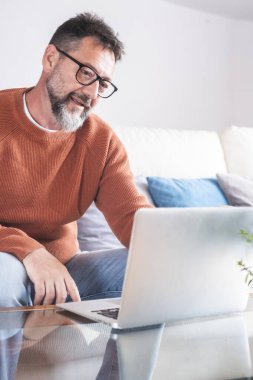 Gülümseyen 50 'li yaşlardaki adam oturma odasında koltukta oturup modern bilgisayar aygıtlarıyla interneti karıştırıyor, evde oturup video sörfü kablosuz ağında mutlu bir serbest çalışan dinleniyor. Ağ aranıyor