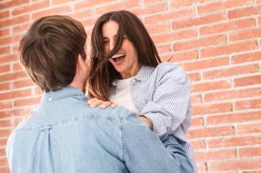 Mutlu genç çift evde birlikte kutluyor, eğleniyor ve çok gülüyor. Erkek, kadını sevgi ve dostlukla kucaklar. Başarı ve başarı kavramı. İçerideki insanlarla ilişki ve flört.