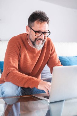 Gülümseyen 50 'li yaşlardaki adam oturma odasında koltukta oturup modern bilgisayar aygıtlarıyla interneti karıştırıyor, evde oturup video sörfü kablosuz ağında mutlu bir serbest çalışan dinleniyor. Ağ aranıyor