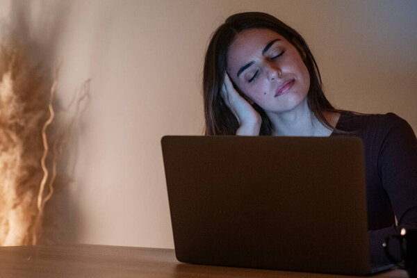 Уставшая деловая женщина, работающая за компьютером до ночи. Портрет стрессовой случайной женщины с головной болью за столом. Уставшая деловая женщина, работающая допоздна на ноутбуке в офисе или дома.