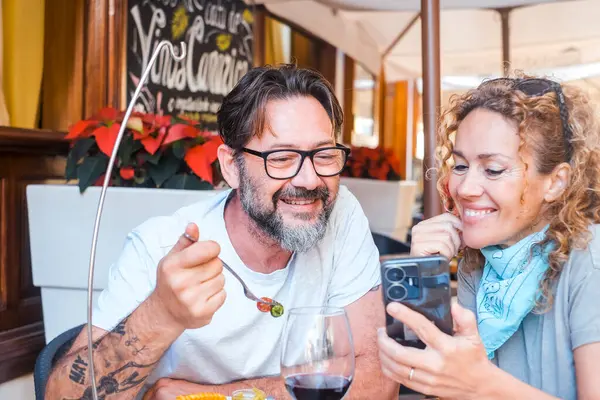 Moderni Aikuinen Pari Näyttää Puhelimen Sisällöstä Istuu Ravintolapöydässä Nauttien Online kuvapankkikuva
