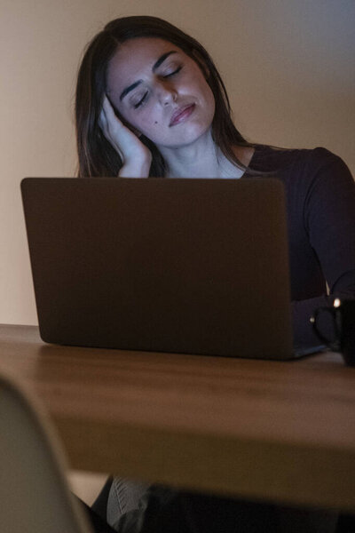 Уставшая деловая женщина, работающая за компьютером до ночи. Портрет стрессовой случайной женщины с головной болью за столом. Уставшая деловая женщина, работающая допоздна на ноутбуке в офисе или дома.