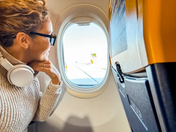 Усміхнений Пасажир Навушниками Bluetooth Який Дивиться Отвору Літака Жінка Середнього Стокове Фото