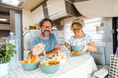 Mutlu bir çift öğle yemeği sırasında bir karavanın içinde eğleniyor. Kampçıları olan insanlar yeni varış noktasını düşünerek gülümsüyor. Erkek ve kadın huzur içinde yemek yiyor.
