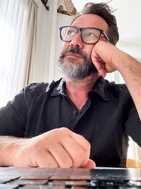 Bir dizüstü bilgisayarın önünde yetişkin bir adam web kamera görüntüsünde, çözümler hakkında hayal kuruyor ve düşünüyor. Fazla mesai. Otel odasında bir iş adamı arkadaşla görüntülü görüşme bekliyor. Çevrimiçi modern iş dünyası