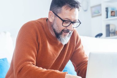 Yetişkin bir adamın kanepeye oturup dizüstü bilgisayara yazı yazışının yan görüntüsü. Alternatif ofis içinde küçük işletme konsepti yaşam tarzı. Modern erkek insanlar kapalı alanda boş zaman aktivitelerinde bilgisayar kullanırlar. İnternete göz atıyorum.
