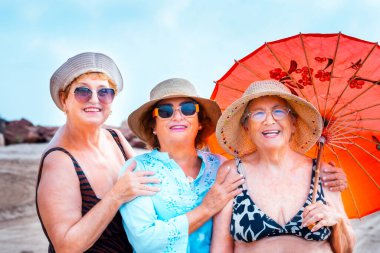 Group of women friends aged smiling and posing for a photo in summer outdoor leisure activity together in friendship. Colorful accessories and sunglasses. Holiday vacation elderly people females ladies clipart