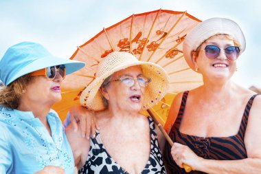 Yazın gülümseyen ve poz veren bir grup kadın arkadaş arkadaşça boş zamanlarında birlikte fotoğraf çekiliyorlar. Renkli aksesuarlar ve güneş gözlükleri. Tatil tatili yaşlı insanlar bayan bayanlar