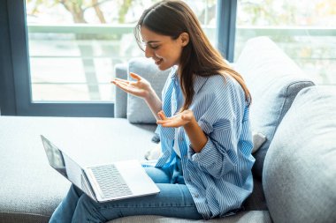 Gülümseyen kadın dizüstü bilgisayar kullanıyor, evdeki koltukta oturuyor, güzel kız sosyal ağlarda sohbet ediyor ve arkadaşlarıyla gülüyor. Teknoloji ve arkadaşlık kavramı..