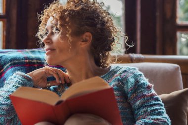  Kadın kitap okuyor sandalyede rahat rahat oturuyor ve dışarı bakıyor düşünüyor ve bekliyor. İnsanlar içeride yalnız zaman geçirmenin keyfini çıkarıyorlar.