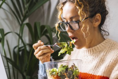 Diyet yapan, şeffaf kaseden taze salata yiyen bir kadın evde dizüstü bilgisayar kullanırken çevrimiçi içeriği izliyor. Çevrimiçi yeni iş konsepti yaşam tarzıyla meşgul genç girişimci. Yemek molası bayan.