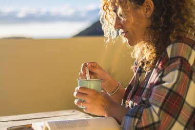 Kıvırcık sarışın kadın terasta masada oturmuş kitap okurken rahatlıyor. Boş zaman ve rahatlama konsepti