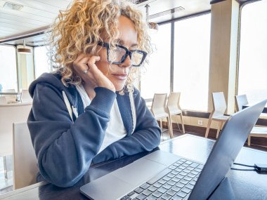 Gemi gezisi sırasında masada oturan güzel sarışın yönetici. Kıvırcık saçlı ve siyah gözlüklü bir kadın seyahat ederken laptop kullanıyor. Dijital göçebeler kavramı.