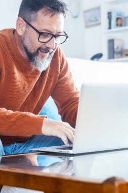 Yetişkin bir adamın kanepeye oturup dizüstü bilgisayara yazı yazışının yan görüntüsü. Alternatif ofis içinde küçük işletme konsepti yaşam tarzı. Modern erkek insanlar kapalı alanda boş zaman aktivitelerinde bilgisayar kullanırlar. İnternete göz atıyorum.