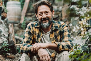 Bahçede oturmuş gülümseyen yetişkin bir adamın kendinden emin portresi. Yetişkin erkek insanlar dışarıda rahatça eğleniyorlar. Mutlu kıdemli gevşemeler. Yere oturun.