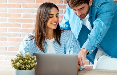 Milenyum çifti masa başında dizüstü bilgisayarda birlikte çalışıyor. Ortak çalışma alanı ve bilgisayar kullanan insanlar. Ortak çalışma konsepti yaşam tarzı. Kadın ve erkek ofiste mutlu bir defter kullanır. İşbirliği işi.