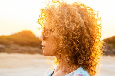 Uzun sarı kıvırcık saçlı bir kadının yaz tatili tatilinde gün batımında dışarı çıkmayı düşünmesi. İnsanlar ve macera yaşam tarzı. Dışarıda, güneş ışığında sağlıklı bir kadın.