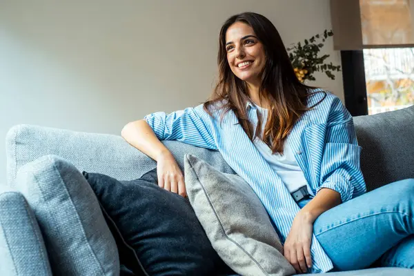 stock image Relax and unwind. Young beautiful brunette woman with blissful facial expression smiles alone on the sofa. Portrait of relaxed woman resting at home.