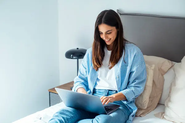 stock image young woman working on laptop and smiling while sitting in living room.