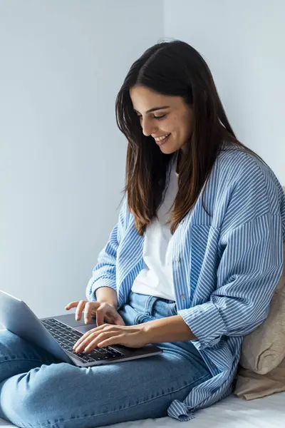 stock image young woman working on laptop and smiling while sitting in living room.