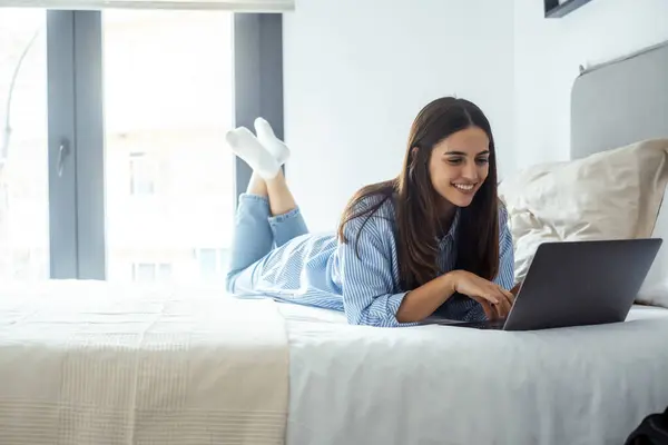 stock image young woman in white shirt and blue jeans is working on the laptop in a cozy apartment.