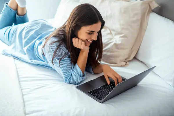 stock image young woman in white shirt and blue jeans is working on the laptop in a cozy apartment.