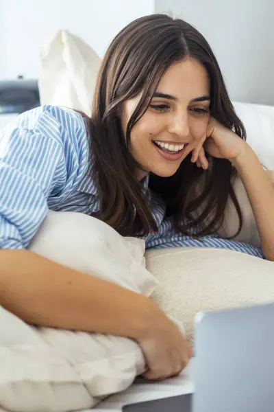 stock image Beautiful happy woman working or watching comedy movie on a laptop lying on bed at home.