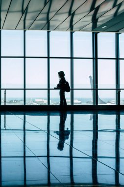 Airport gate and people waiting to fly. Silhouette tourist woman standing and looking outside at the aircraft. People on vacation or business trip. Travel lifestyle and mirror on the floor. Tourism