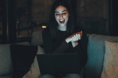 Genç ve güzel bir kadın, gece geç saatlerde evinde ekranı açık olan bir bilgisayarla video görüşmeleri yapıyor. Gülümseyen kız internette ailesi ve arkadaşlarıyla konuşurken gülümsüyor ve jestler yapıyor. Sosyal medya