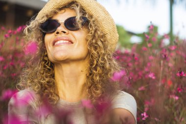 Happy woman smile and enjoy sitting in the middle of pink meadow blossom flowers enjoying spring and outdoor leisure activity alone. Excited and joyful female people with positive lifestyle