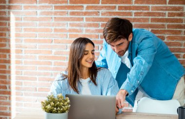 Milenyum çifti masa başında dizüstü bilgisayarda birlikte çalışıyor. Ortak çalışma alanı ve bilgisayar kullanan insanlar. Birlikte çalışma konsepti yaşam tarzı. Kadın ve erkek ofiste mutlu bir defter kullanır. İşbirliği işi.