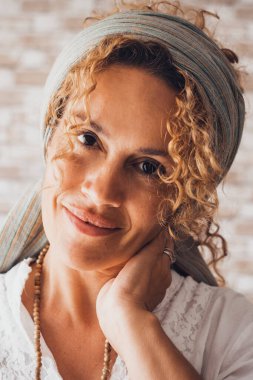 Mutlu kıvırcık kadın kameraya bakarak gülümsüyor. Ev içinde tuğlaları olan orta yaşlı bir kadının ön portresi. Şirin bir kadın sana gülümseyip bakıyor. Neşeli bayan.