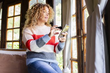  Yetişkin bir kadın evde yalnız başına telefon okuyup mesaj yolluyor.