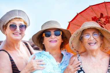 Yazın gülümseyen ve poz veren bir grup kadın arkadaş arkadaşça boş zamanlarında birlikte fotoğraf çekiliyorlar. Renkli aksesuarlar ve güneş gözlükleri. Tatil tatili yaşlı insanlar bayan bayanlar