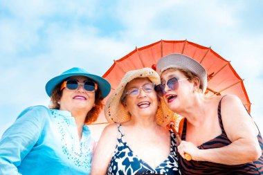 Yazın gülümseyen ve poz veren bir grup kadın arkadaş arkadaşça boş zamanlarında birlikte fotoğraf çekiliyorlar. Renkli aksesuarlar ve güneş gözlükleri. Tatil tatili yaşlı insanlar bayan bayanlar