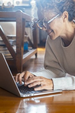  Evde dinlenen bir kadın dizüstü bilgisayarda evde yalınayak yere uzanmış yazıyor. Alternatif uzaktan çalışan ve zeki çalışan kadın yetişkin yaşam tarzı. Web Ara